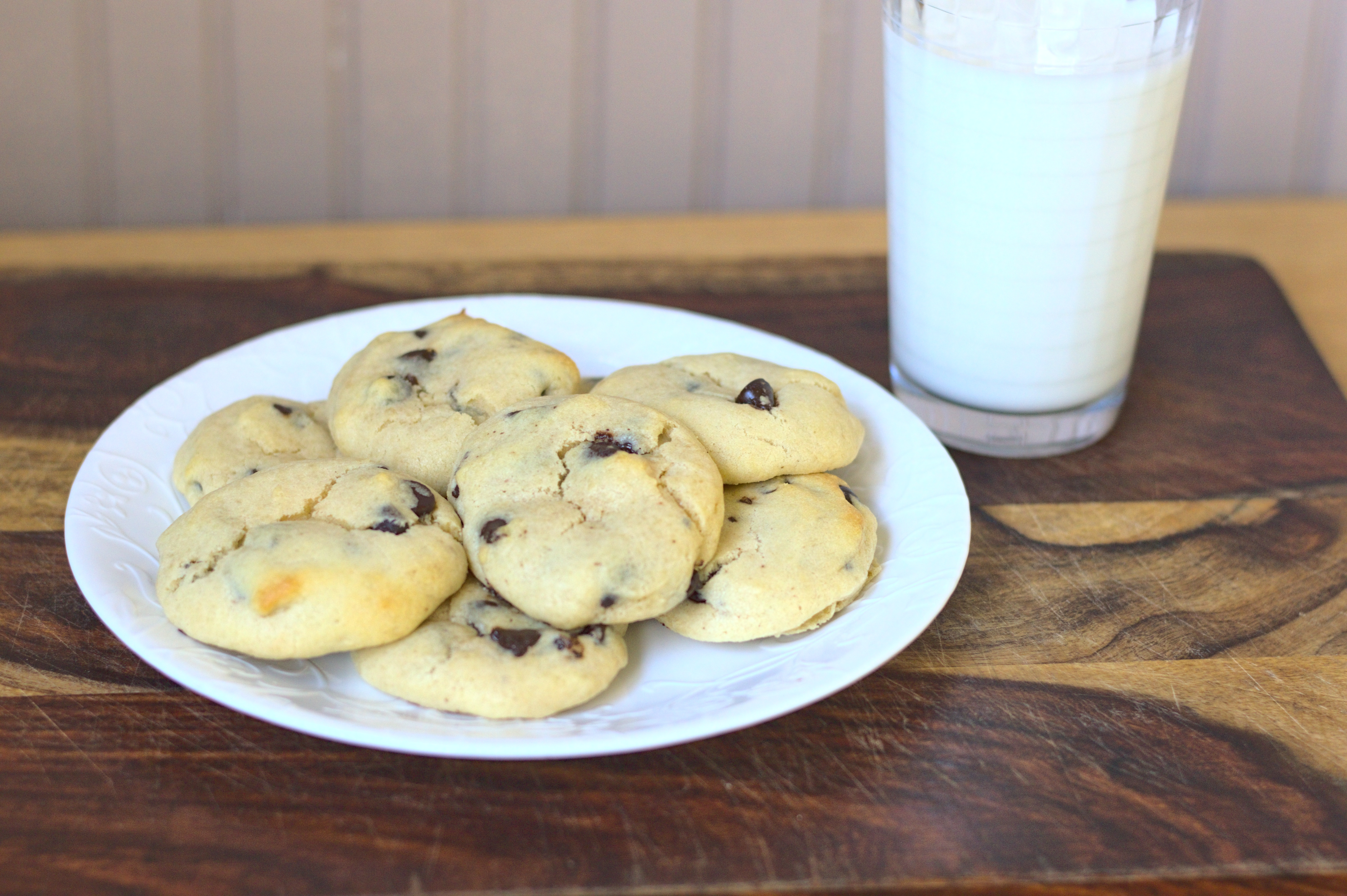 a plate of high protein chocolate chip cookies sit beside a glass of milk.